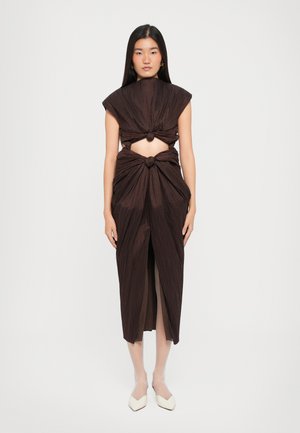 Rochie maro plisată, cu un design nod la talie și la umeri, cu părți laterale deschise și o fanta în față. Modelul stă pe un fundal neutru.