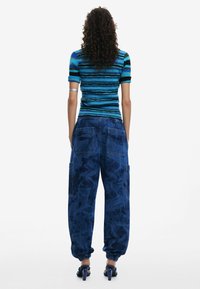 Haut tricoté rayé bleu et noir à manches courtes associé à un pantalon cargo ample, texturé et bleu foncé, avec des chaussures à talons hauts.