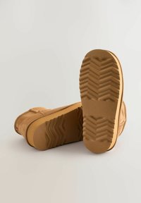 Hnedé semišové čižmy s plochou, štruktúrovanou gumovou podrážkou so zigzagovými vzormi. Dizajn je minimalistický s okrúhlou špičkou a prešitím.