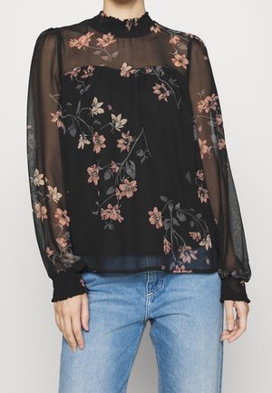 Schwarze durchsichtige Bluse mit langen Ärmeln, rosa Blumenmuster, gerafftem hohen Kragen und Manschetten, kombiniert mit hellblauen Jeans.