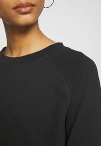 Sweat-shirt noir avec un col ras du cou côtelé et des manches raglan, fabriqué en coton doux avec une texture lisse.