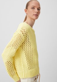 Gelber gestrickter Pullover mit offener Maschenstruktur, Rundhalsausschnitt und gerippten Bündchen. Lockere Passform mit fallenden Schultern und strukturiertem Detail.