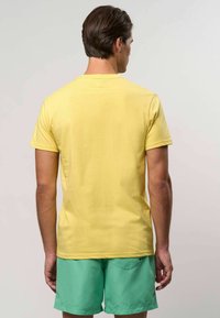 Kollane lühikeste varrukatega t-särk pehmest kangast, millel on puhas ja lihtne disain. Selg on sile, ilma nähtavate logode või mustriteta.