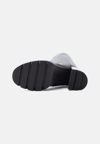 Suela de goma negra con un dibujo texturizado, diseñada para la tracción. Material superior liso con un acabado mate y forma redondeada.