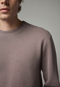 Pull léger violet avec un design en tricot texturé, doté d'un col rond côtelé et de manches légèrement larges.