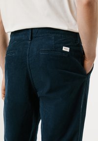 Pantalones de pana en color navy con una superficie texturizada, dos bolsillos traseros y una pequeña etiqueta de la marca en la cintura. Apta para el uso casual.
