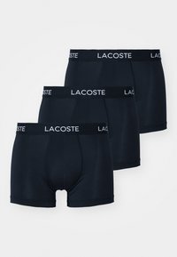 Boxer-briefs bleu marine, paquet de trois. Tissu lisse, ceinture élastique avec logo "LACOSTE" en blanc. Coupe mi-longue avec ajustement près du corps.