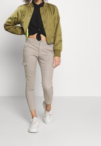 Olivově zelená bomber bunda s žebrovanými manžetami, spárovaná s světlými béžovými cargo kalhotami se bočními kapsami a bílými teniskami.