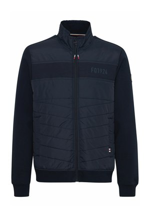 Jūras spēku jaka ar rāvējslēdzēja priekšpusi, quiltētiem paneļiem un ribinātiem piedurkņu galiem. Iezīmēta ar logotipa detaļām uz krūtīm un svītrām apakšmalā.