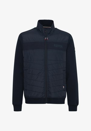 Tamsiai mėlyna striukė su užtrauktuku priekyje, su kvadratiniais siuvinėjimais ir banguotais rankogaliais. Ant krūtinės yra logotipo detalė ir dryžuoti akcentai apačioje.