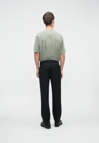 Camicetta grigia a maniche corte realizzata in tessuto morbido, abbinata a pantaloni neri. L'outfit ha una vestibilità rilassata, con cuciture minime e uno stile classico.