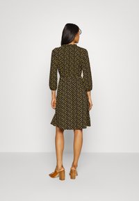 Vestido preto com bolinhas amarelas, mangas compridas, cintura justa e saia rodada. Usado com sapatos de salto bloco castanhos.