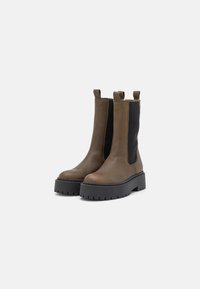 Bottines en cuir marron avec des panneaux latéraux élastiques, des accents noirs et une semelle plateforme épaisse noire. Comprend deux languettes de tirage pour un enfilage facile.