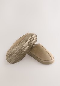 Chaussons en daim beige avec une semelle profilée basse, un bout rond, et des coutures décoratives, dotés d'une semelle en caoutchouc texturée avec un motif en zigzag.