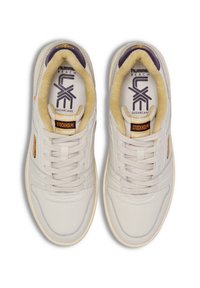 Baskets blanches avec une finition lisse, une forme arrondie et des accents beiges. L'étiquette indique "hummel REACH SUGAR CANE STOCKHOLM." Doublure douce et rembourrée.