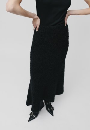 Black long skirt made of textured, fuzzy fabric with a fitted waistband. Paired with pointed black shoes featuring buckled accents.