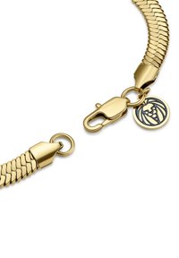 Gulltonet metallarmbånd med et fleksibelt, teksturert kjededesign, en fjærkrok og en charm med et løveemblem.