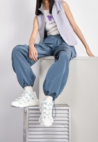 Nike ärmlös jacka i ljusgrå över en vit grafisk topp. Blå tapered joggers och vita sneakers med mintdetaljer. Slät tygtextur.