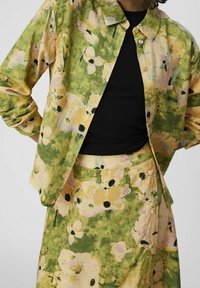 Veste chemise à imprimé floral dans des teintes vertes, jaunes et roses, dotée d'une coupe décontractée, d'une fermeture à boutons et d'un tissu léger et doux. Associée à une jupe assortie.