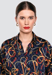 Bluzka wykonana z materiału z nadrukiem, w granatowym kolorze, z motywami złotych, czerwonych i niebieskich łańcuchów oraz frędzli. Z kołnierzykiem, z zapięciem na guziki.