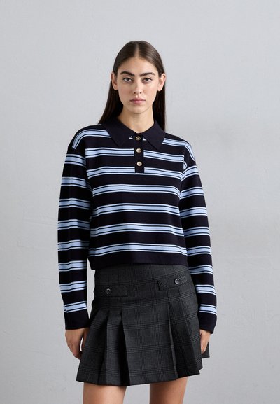 Suéter de cuello con rayas azul marino y azul claro, con cuatro botones dorados, combinado con una falda plisada de cuadros negra que cuenta con bolsillos laterales y acentos de botones.