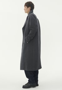 Grå ullrock med lös passform, enkelknäppt design och två sidofickor. I kombination med mörka jeans och svarta snörstövlar.