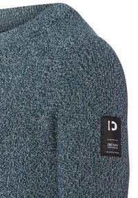 Pullover aus strukturiertem Strickstoff in Blau- und Grautönen, mit einem schwarzen Etikett mit Logo und Markennamen am Ärmel.