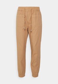 Beige cotton jogger pants with an elastic waistband, adjustable drawstring with metal ends, and two side pockets. Slim fit with elastic cuffs.