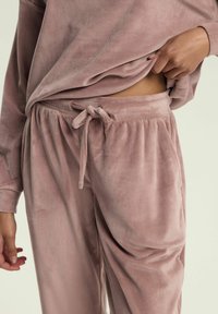 Miękki różowy, aksamitny zestaw odzieży domowej z regulowanym stanem i luźnymi spodniami. Długi rękaw bluzki w luźnym kroju z prążkowanymi mankietami.