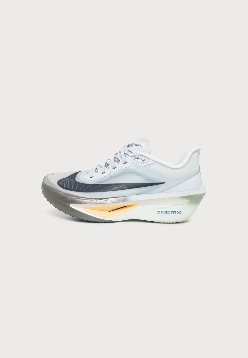 Λευκό και γκρι παπούτσι τρεξίματος Nike Zoom Fly με μαύρο λογότυπο και παχύ μαξιλάρι στην σόλα με κίτρινο στοιχείο σε μονόχρωμο φόντο.