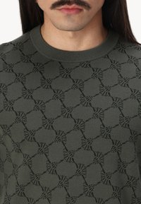 Olivgrüner, gestrickter Pullover mit einem sich wiederholenden geometrischen Muster in dunkleren Farbnuancen, Rundhalsausschnitt und strukturiertem Stoff.