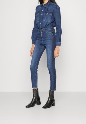 Dżinsowa koszula z dwoma kieszeniami, długimi rękawami i zapięciem na guziki. Dopasowane ciemnoniebieskie jeansy z bocznym detalem, w połączeniu z czarnymi botkami za kostkę.