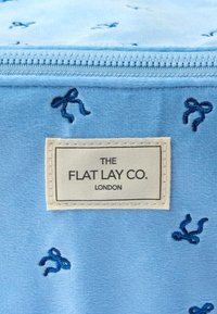 Bolsa de tela azul clara con diseños de lazo bordados en azul oscuro, que presenta una etiqueta rectangular con "THE FLAT LAY CO. LONDON."