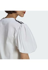 Top blanco de manga corta con mangas abullonadas, escote redondo y rayas negras de acento a lo largo de los hombros. Textura de algodón suave.