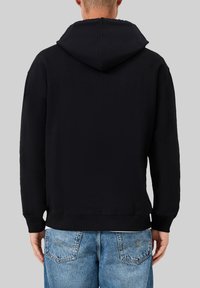 Zwarte hoodie met een ontspannen pasvorm, zachte stof en een trekkoordcapuchon. Het heeft ribgebreide manchetten en een zoom, gecombineerd met lichtblauwe jeans.