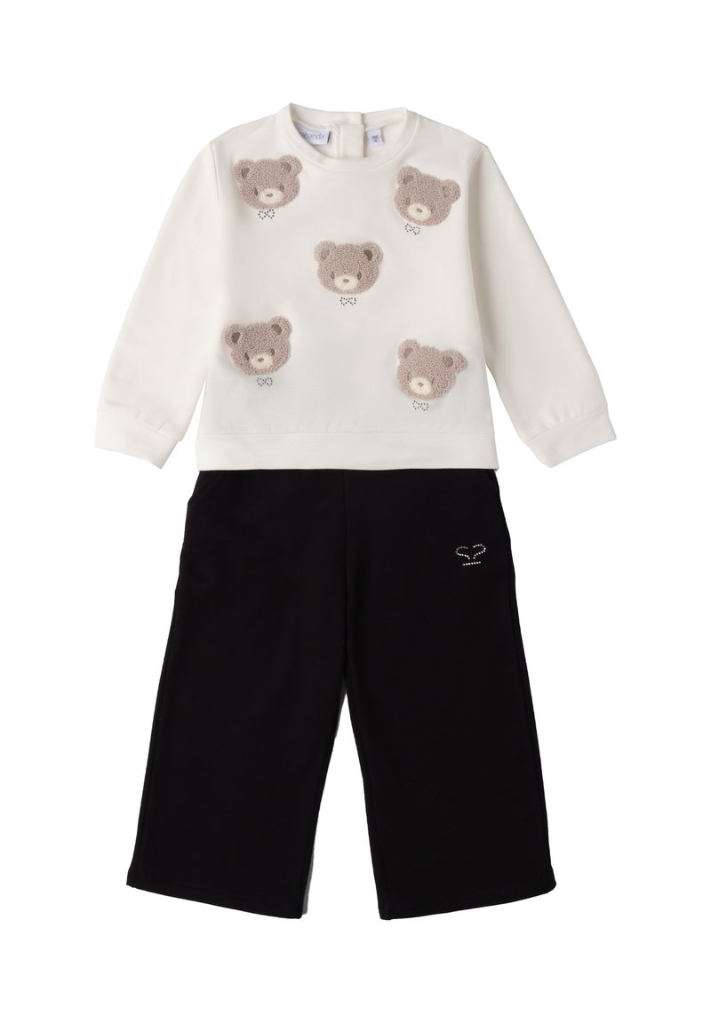 Biała bluza z pięcioma fakturowanymi aplikacjami w kształcie misiów, zestawiona z czarnymi spodniami o szerokich nogawkach z małym haftem na kieszeni.