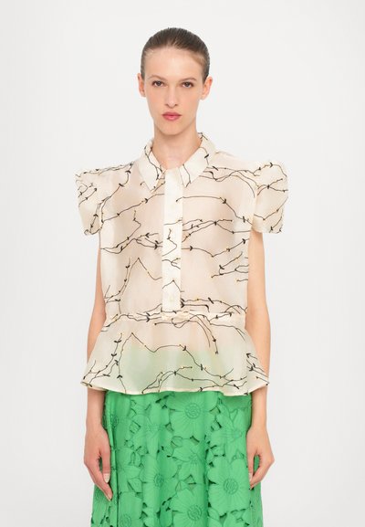 Bluse aus transparentem beigen Stoff mit schwarzem Zweigmuster, kurzen Puffärmeln und Knopfleiste. Kombiniert mit einem grün strukturierten Rock.
