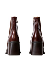 Bottines en cuir bordeaux avec une finition brillante, un talon carré et une fermeture éclair à l'arrière ; présentant une texture côtelée sur les côtés.