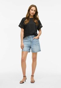 Top nero a maniche corte con dettagli testurizzati neri abbinato a pantaloni corti in denim azzurro chiaro e tacchi neri con cinturini. Outfit casual per il clima caldo.