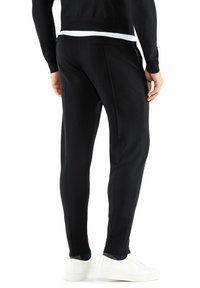 Zwarte op maat gemaakte broek met een slim fit, gemaakt van zachte stof. Bevat twee achterzakken en naadloze zijdetails, gecombineerd met witte sneakers.
