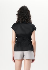 Sort bluse med korte ærmer, indsnævret talje og høj krave, lavet af glat materiale med en afslappet pasform, parret med lyse grå shorts.