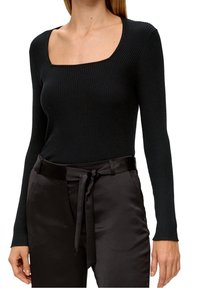 Top negro de manga larga con relieve y escote cuadrado, combinado con pantalones de satén negros que cuentan con un detalle de lazo en la cintura.