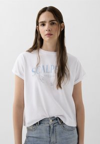 Witte katoenen T-shirt met opgerolde korte mouwen, met het woord "SCALPER" in lichtblauw en vleugeldiagrammen. Gekocht met hoge taille denim jeans.