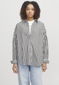 Stribet skjorte i sort og hvid med krave, forlommer og manchetter, båret over en hvid top. Kombination med lyse denim jeans.
