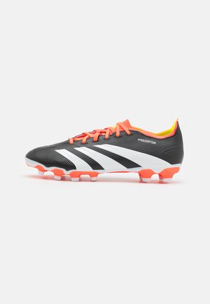 Chaussure de football noire avec des rayures blanches, des accents orange, une surface texturée et des crampons en caoutchouc. Présente un col rembourré pour plus de confort.