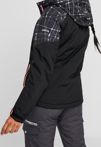 Schwarze wasserdichte Jacke mit einem karierten Oberteil in Schwarz und Weiß, pinken Akzenten, Reißverschlusstaschen und Velcro-Bündchen.