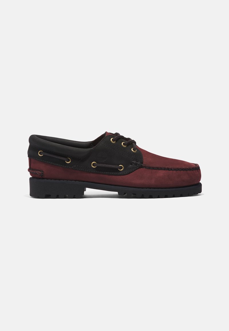 Zapato de barco de cuero burdeos y negro para hombre con cordones negros, ojales dorados, cuello acolchado y suela de goma negra texturizada.