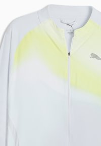 Chaqueta blanca con cremallera y un sutil degradado amarillo en el pecho, con un logo gris de Puma en el lado derecho.