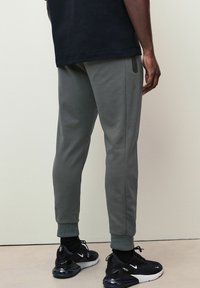Graue Jogginghose mit schmalem Schnitt, strukturiertem Stoff und gerippten Bündchen. Kombiniert mit schwarzen Sportschuhen, die eine sichtbare Luftpolsterung aufweisen.