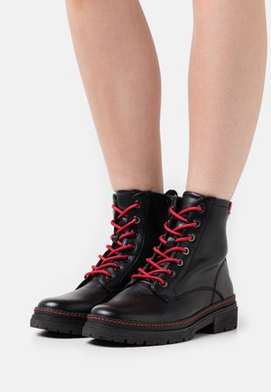 Zwarte leren enkellaarzen met rode veters, voorzien van een ritssluiting aan de zijkant, een rubberen zool met structuur en rode stiksels langs de zool.